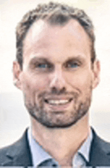 a man with a beard is smiling for the camera while wearing a suit and tie .