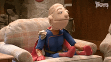 a puppet in a superhero costume is sitting on a couch with the boys logo in the background