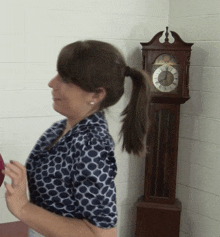 a woman is standing in front of a grandfather clock that shows the time as 4:20