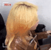 a woman with blonde hair is sitting in front of a camera with a red rec button .