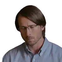 a man wearing glasses and a blue shirt looks down with his eyes closed