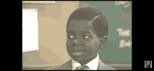 a young boy in a suit and tie is standing in front of a blackboard