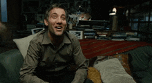 a man is sitting on a couch laughing with a cat on his lap