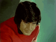 a man in a red sweater with white stripes on the sleeves looks at the camera