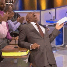 a man in a suit and tie is laughing while holding a piece of paper in front of a group of people .