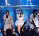 a woman in a white dress is singing into a microphone in front of a crowd at a concert .