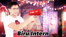 a man holding a red object with the words biru intern written on it