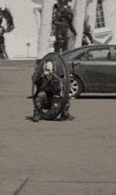a man is sitting on a wheel in a parking lot next to a car