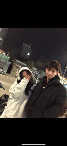 a boy and a girl are standing next to each other and the girl is covering her face