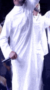 a man in a white robe is singing into a microphone on stage