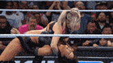 two women are wrestling in a ring with a crowd watching and one has a tattoo on her arm