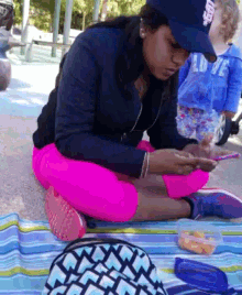 a woman sitting on a blanket looking at her phone with a girl in a blue shirt behind her