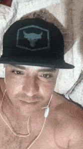 a shirtless man wearing a black hat and ear buds is laying on a bed .