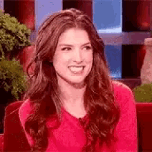 a woman in a red sweater is sitting on a red couch and smiling .