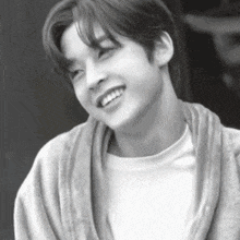 a black and white photo of a young man smiling while wearing a sweater .