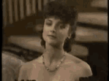 a woman wearing a necklace and earrings is standing in a room .