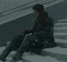 a man is sitting on a set of stairs covered in snow .