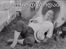 a black and white photo of a man laying on the ground with a hat on ..