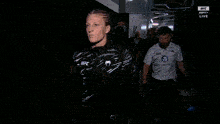 a woman wearing a jacket that says ufc is walking through a dark room