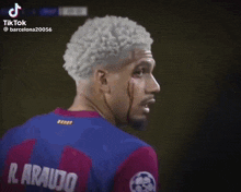 a soccer player with white hair is standing in front of a purple background .