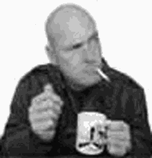 a man is sitting at a table smoking a cigarette and drinking a beer .