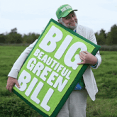a man in a green hat is holding a green sign that says big beautiful green bill