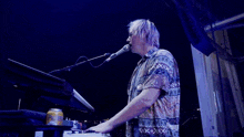 a man singing into a microphone while playing a keyboard with a can of bud light on the table