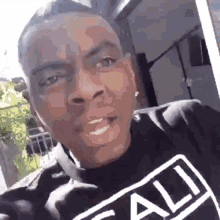 a man wearing a black t-shirt with the word ali on it is making a funny face .