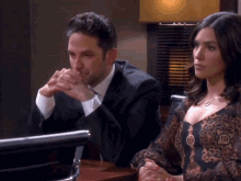 a man and a woman are sitting at a desk with their hands folded