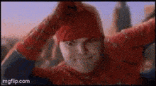 a man in a spiderman costume is scratching his head and smiling .