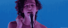 a man with curly hair is singing into a microphone without a shirt on .
