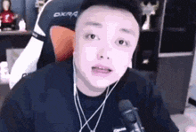 a man wearing headphones and a necklace is sitting in front of a microphone and making a funny face .