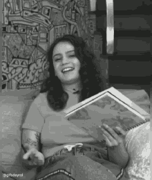 a woman is sitting on a couch holding a book and smiling