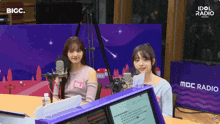two girls are sitting in front of a mbc radio station