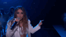 a woman is singing into a microphone on a stage while a group of women are dancing behind her .