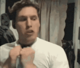 a man in a white shirt is tying a tie in a room .