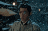 a man in a kimono is standing in the snow and looking at the camera .