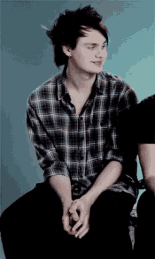 a young man in a plaid shirt is sitting next to another young man holding hands .