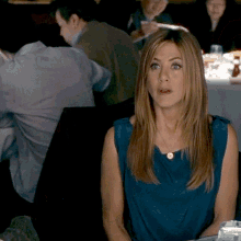 a woman in a blue top sits at a table in a restaurant