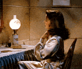 a woman sits at a table with a lamp and brush