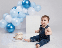a baby is sitting in front of a cake with balloons behind him