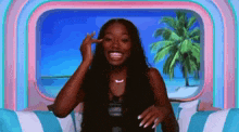 a woman is sitting on a couch with a palm tree in the background and smiling .