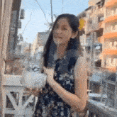 a young woman in a floral dress is standing on a balcony holding a bowl .