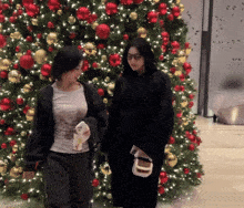 two women standing in front of a christmas tree holding hands