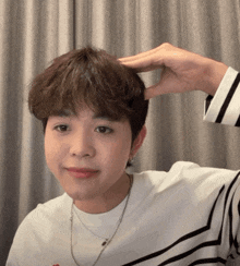 a young man wearing a striped shirt has his hand on his forehead