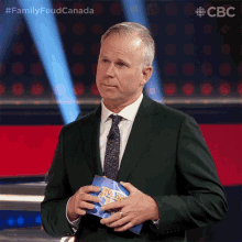 a man in a suit and tie is holding a piece of paper that says " family feud canada "