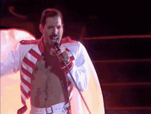 a shirtless man singing into a microphone while wearing a red and white jacket