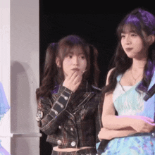 two girls are standing next to each other with one wearing a plaid jacket and the other wearing a blue dress