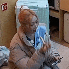 a woman is sitting on the floor with a suitcase in the background eating a sandwich .