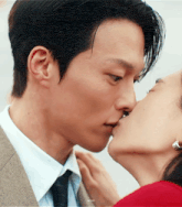 a man in a suit and tie kisses a woman in a red shirt